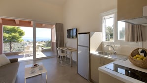 Een compacte keuken met een koelkast, wastafel en eethoek. Een televisie is aan de muur bevestigd, en er is een balkon met uitzicht op zee.