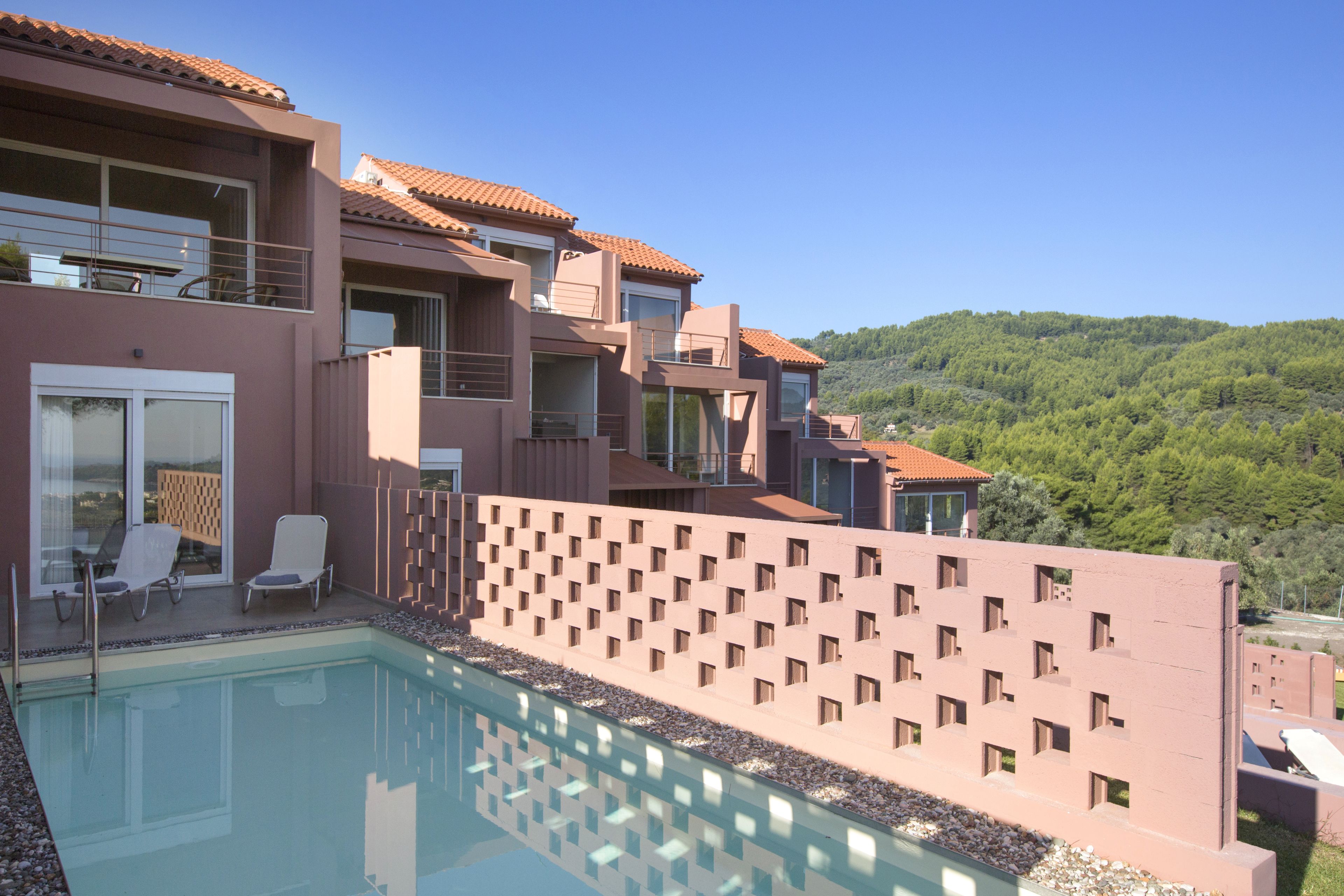 Un hotel moderno con piscina, varios balcones y vistas a una colina verde.