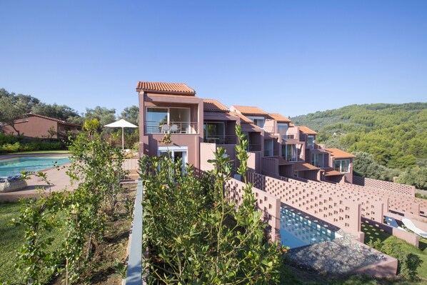 A modern multi-story house with a swimming pool, surrounded by lush greenery and hills.