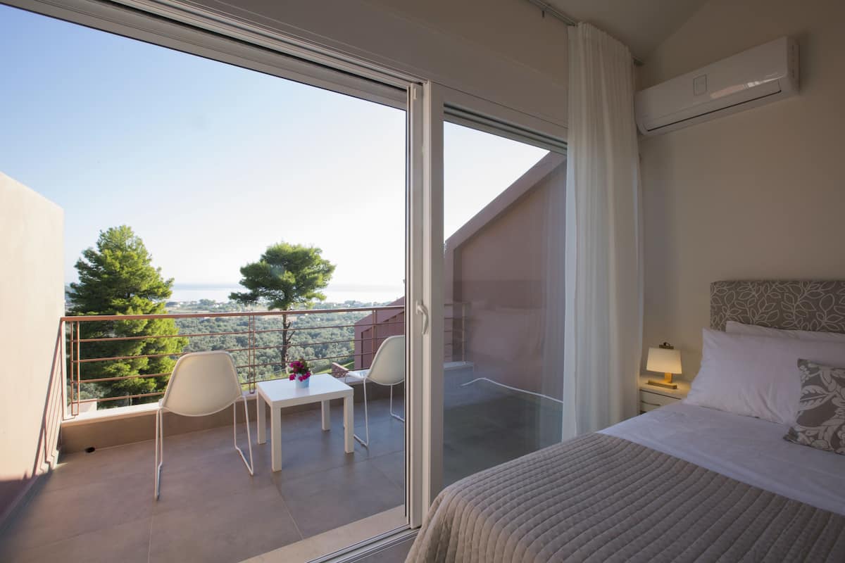 A bedroom with a balcony, a bed, a nightstand, and a view of the city.