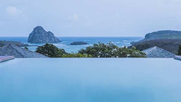 A infinity pool with a view of the ocean and a rocky island. - Pousada Maravilha Fernando de Noronha (Fernando de Noronha)