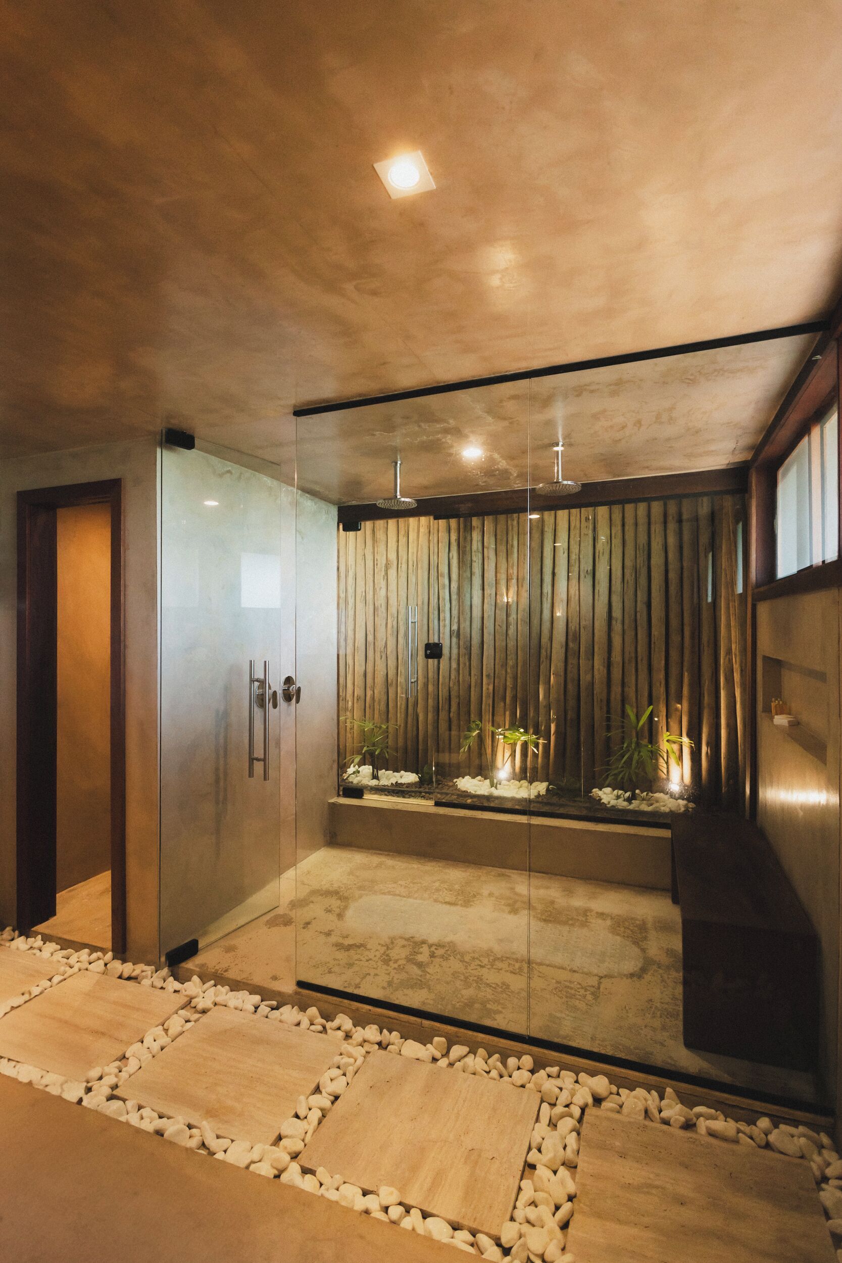 A modern bathroom with a glass shower enclosure, wooden panel wall, and a stone-tiled floor.
