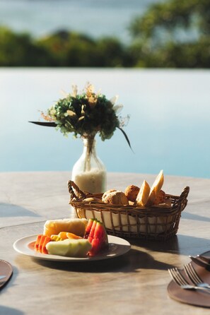 A dining table with a basket of bread and a plate of fruit.