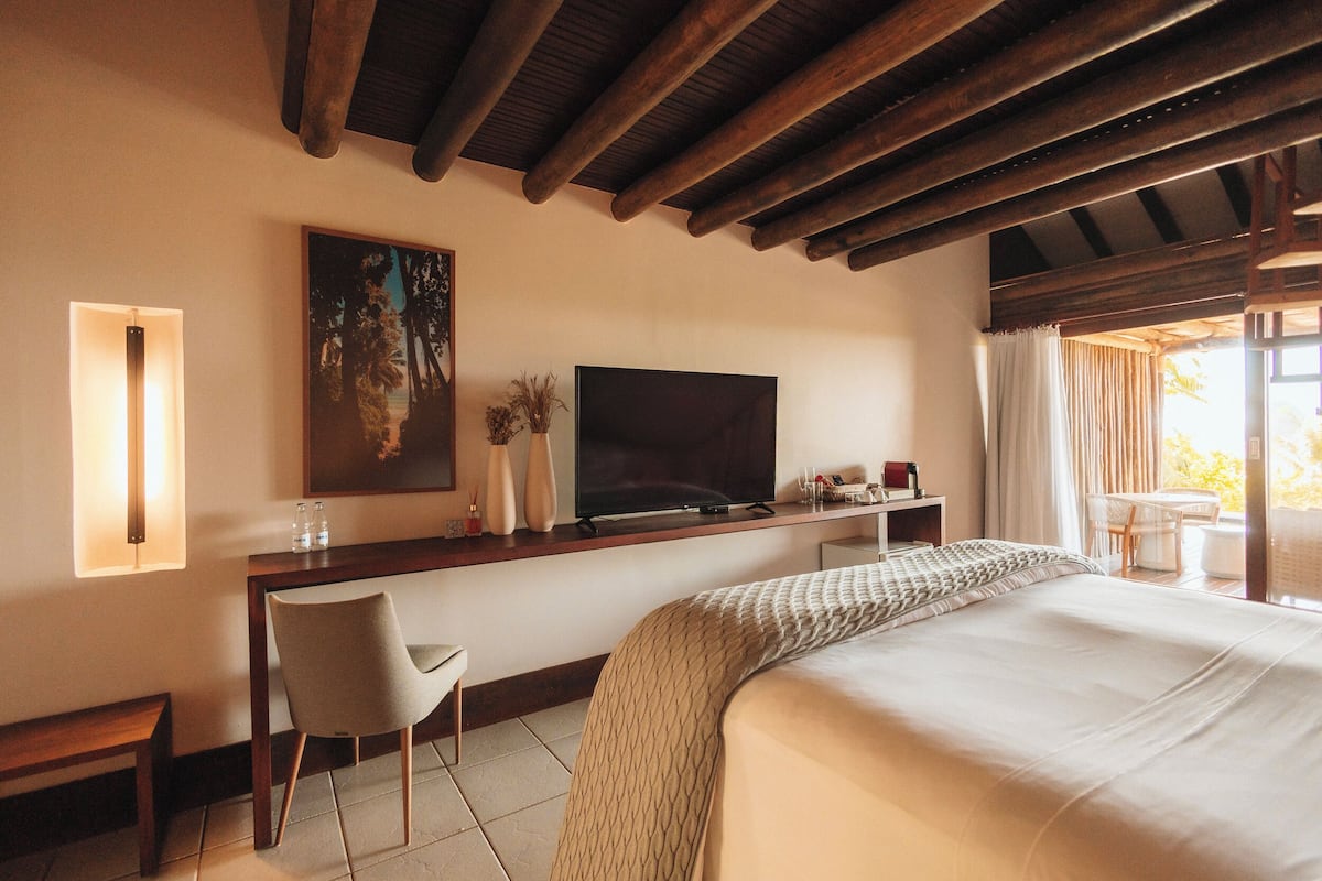 A hotel room with a large bed, a desk with a TV, a chair, and a window with curtains.