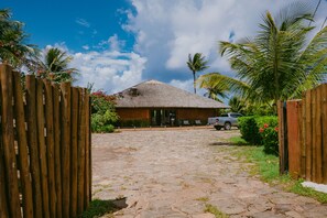 A rustic building with a thatched roof, surrounded by a wooden fence and palm trees.