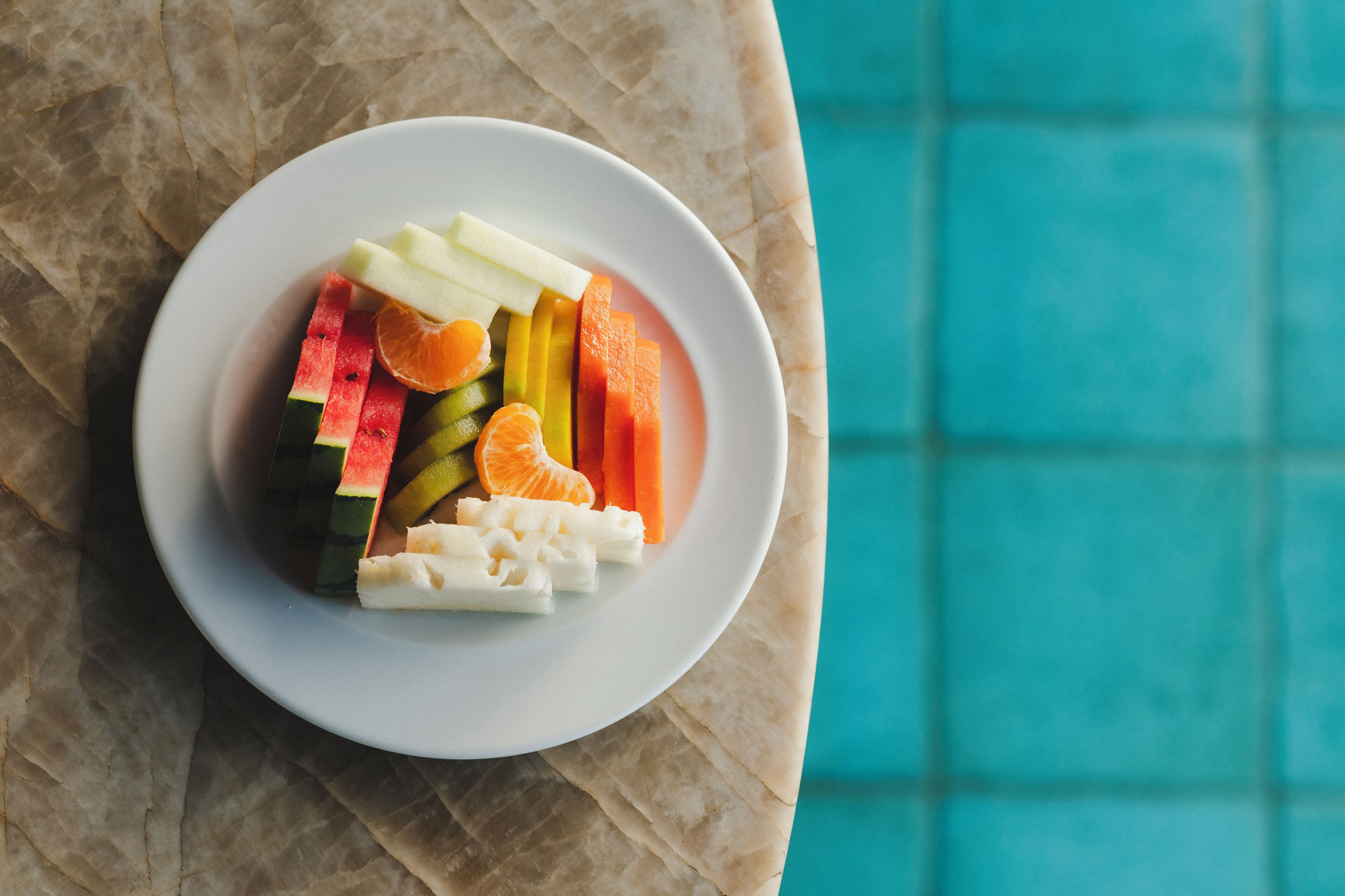 A white plate with sliced fruits and vegetables on a table.