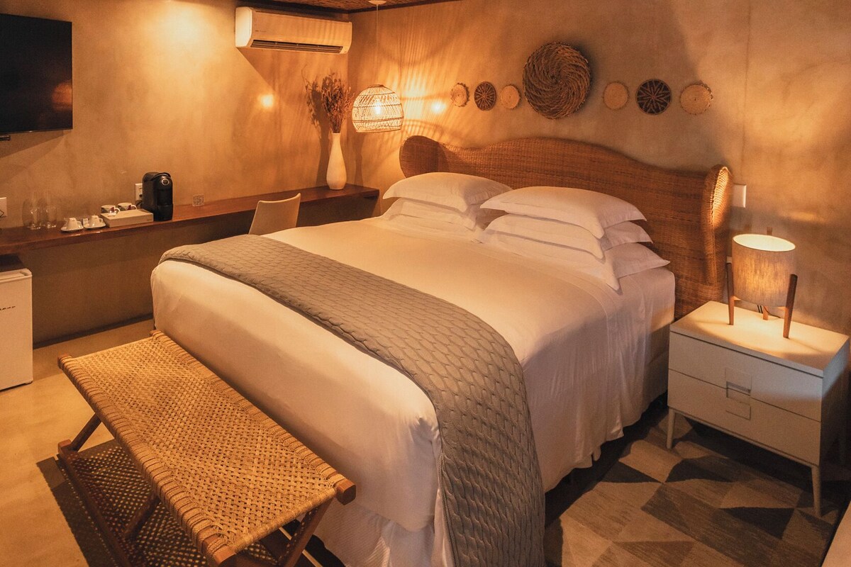 A bedroom with a large bed, bedside tables, a bench, a TV, and a ceiling with a woven pattern.
