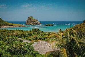 A coastal landscape with a prominent rock formation, lush greenery, and a clear view of the ocean.