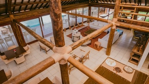 A spacious indoor area with a wooden ceiling and large windows, featuring a dining area with tables and chairs, a sofa, and a small kitchen area. - Pousada Maravilha Fernando de Noronha (Fernando de Noronha)
