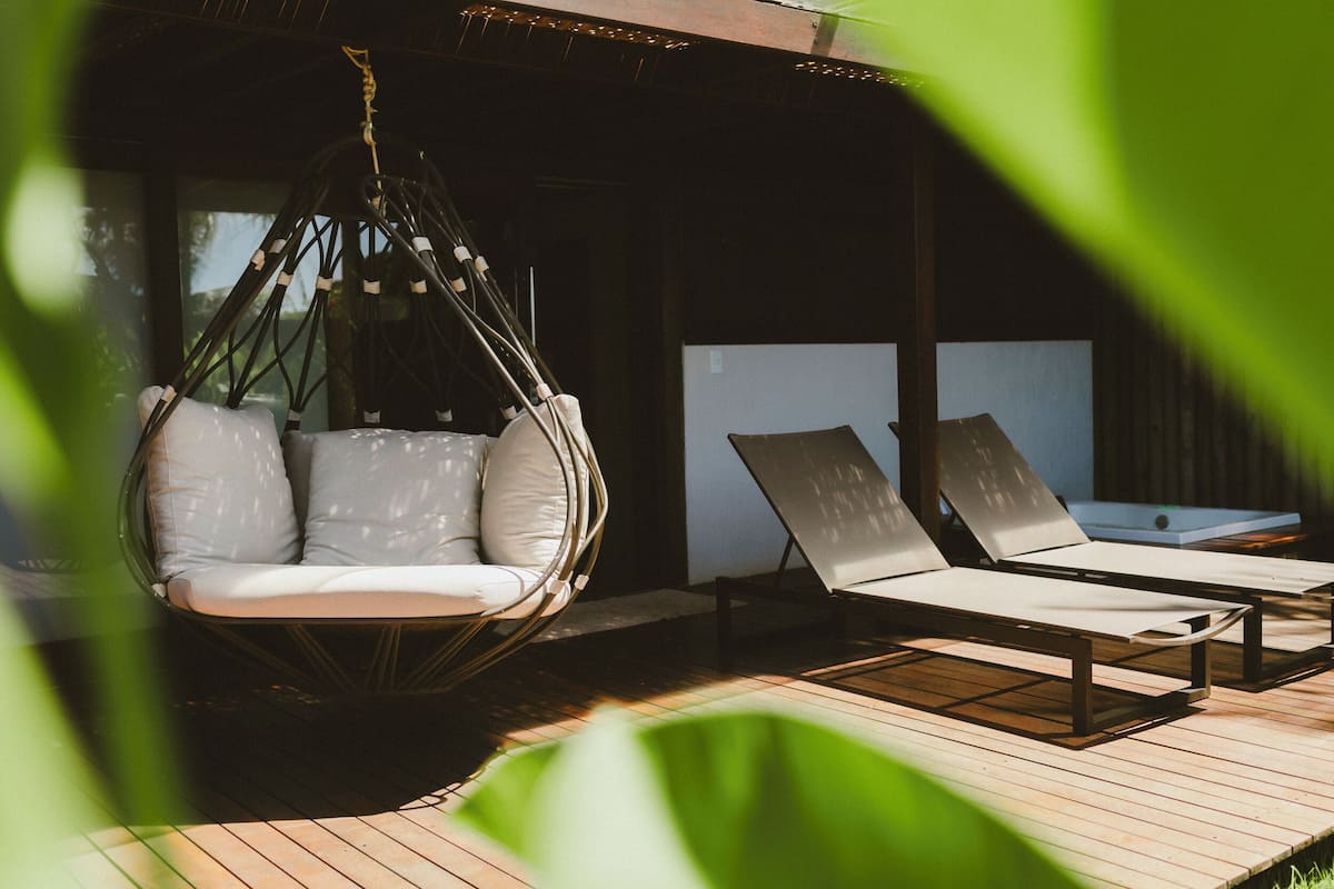A wooden deck with a hanging chair and two lounge chairs.