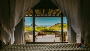 A bedroom with a large window overlooking a deck with a view of the ocean and greenery. - Pousada Maravilha Fernando de Noronha (Fernando de Noronha)