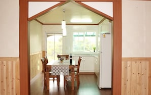 A dining area with a table and chairs, a refrigerator, and a window with a view of greenery.