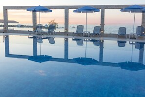An infinity pool with lounge chairs and umbrellas, overlooking a body of water at sunset. - Porto Alegre (Chania)