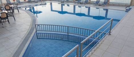 Una piscina con sillas de descanso y sombrillas, rodeada por una terraza de baldosas y con vista a una extensión de agua.