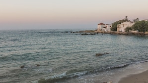 A coastal scene with a sandy beach, calm sea, and buildings with white walls and red roofs. - Porto Alegre (Chania)