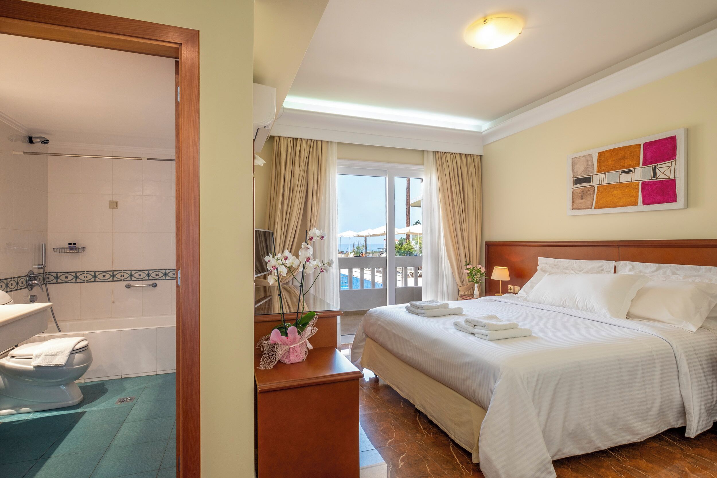 Une chambre d’hôtel avec un grand lit, une salle de bain avec douche et un balcon offrant une vue sur la mer.