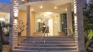 The entrance of Porto Alegre hotel with multiple flags, a staircase, and a well-lit facade. - Porto Alegre (Chania)