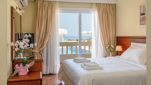 A hotel room with a bed, a desk, a mirror, a window with curtains, a view of the sea, and a balcony with umbrellas. - Porto Alegre (Chania)