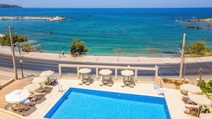 A swimming pool with lounge chairs and umbrellas, overlooking a coastal area with clear blue water and rocky outcrops. - Porto Alegre (Chania)