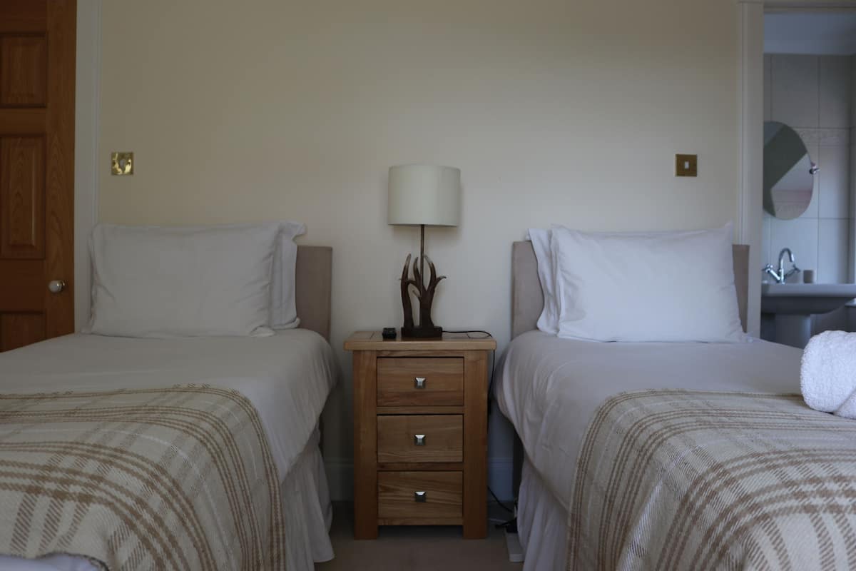 A hotel room with two beds, a bedside table with a lamp, and a bathroom visible through an open door.