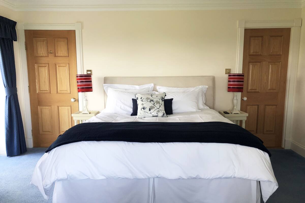 A neatly made bed with white bedding and a black throw blanket, flanked by two bedside tables with lamps, in a room with wooden doors and a plain wall.
