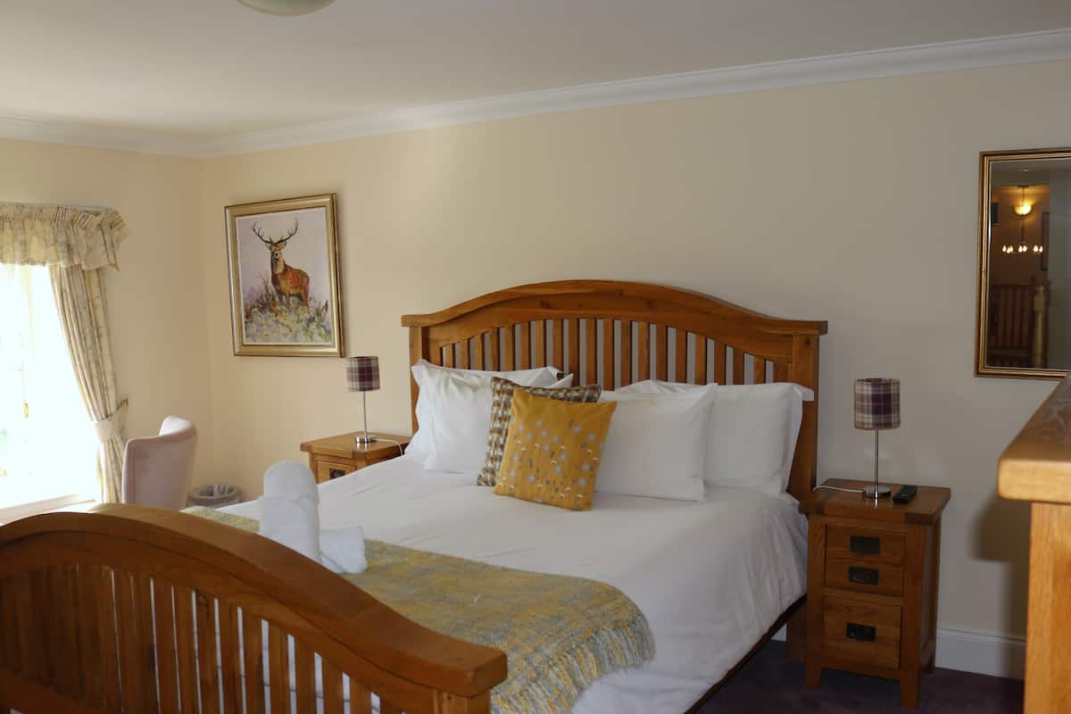 A neatly made bed with a wooden headboard, two bedside tables with lamps, a chair, a painting on the wall, and a mirror.