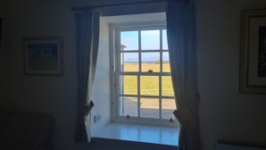 Ein Zimmer mit großem Fenster, Vorhängen, einem gerahmten Bild an der Wand und einer Heizung.