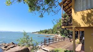 A coastal property with a wooden deck, large rocks, and a view of the sea. - Pousada Prainha da Nina (Florianópolis)
