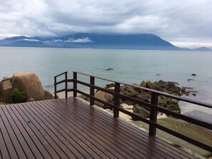Una terraza de madera con barandilla que da a una masa de agua tranquila y montañas a la distancia.