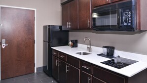 Una cocina con armarios de madera oscura, un refrigerador negro, un microondas, un fregadero y una placa de inducción.