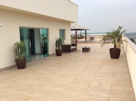 Una terraza en la azotea con plantas en macetas, mobiliario exterior y una entrada con puerta de cristal.