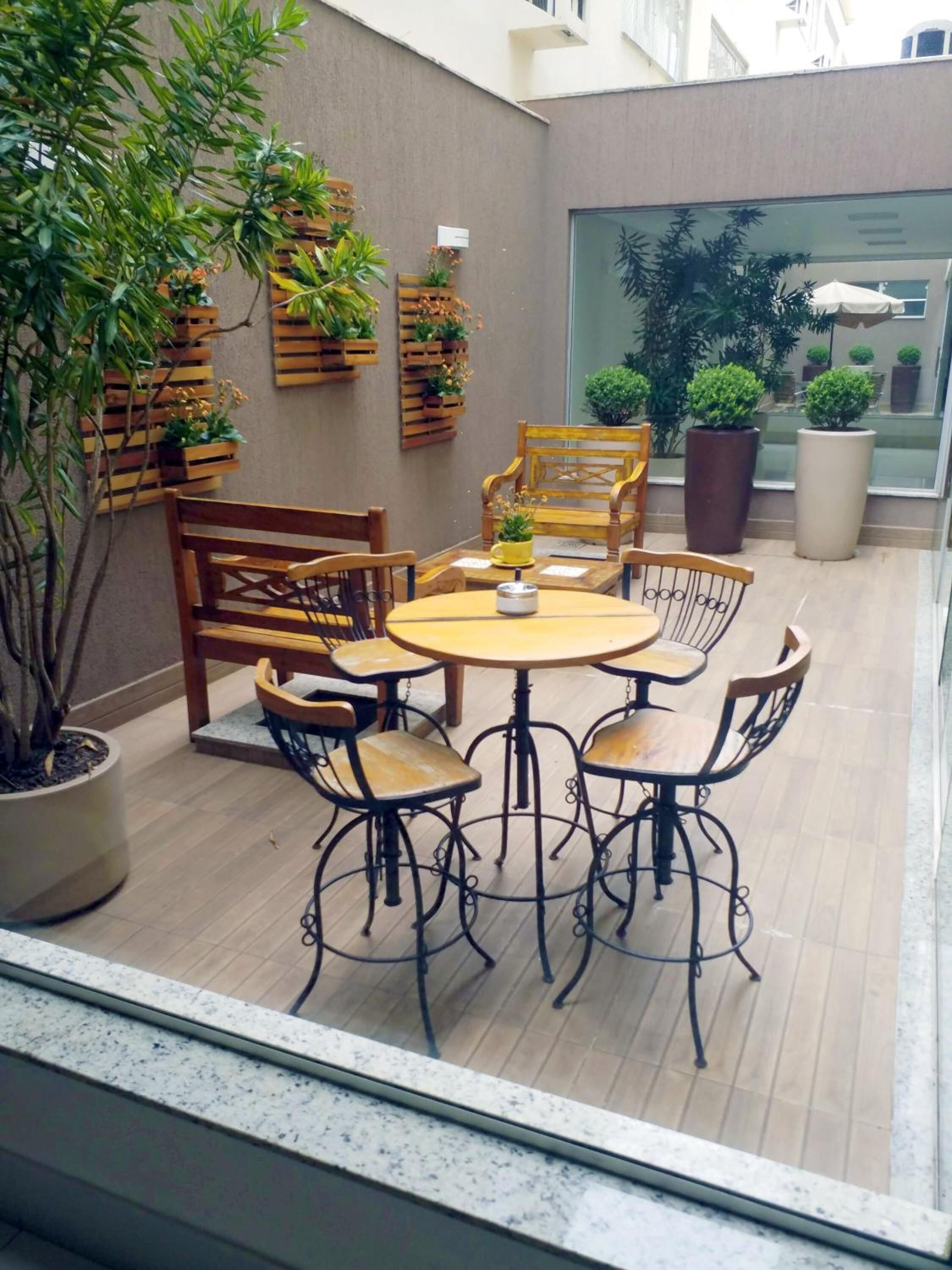 Un patio con una mesa redonda y seis sillas, rodeado de plantas en macetas y mobiliario de madera.