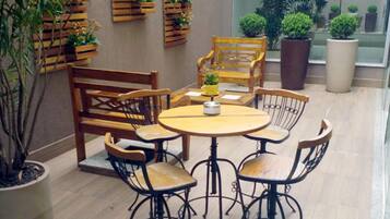 Un patio con una mesa redonda y seis sillas, rodeado de plantas en macetas y mobiliario de madera.