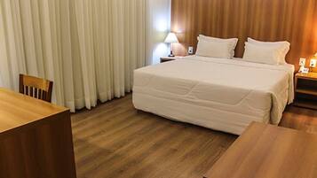 A hotel room with a large bed, wooden floor, a desk, and a chair.