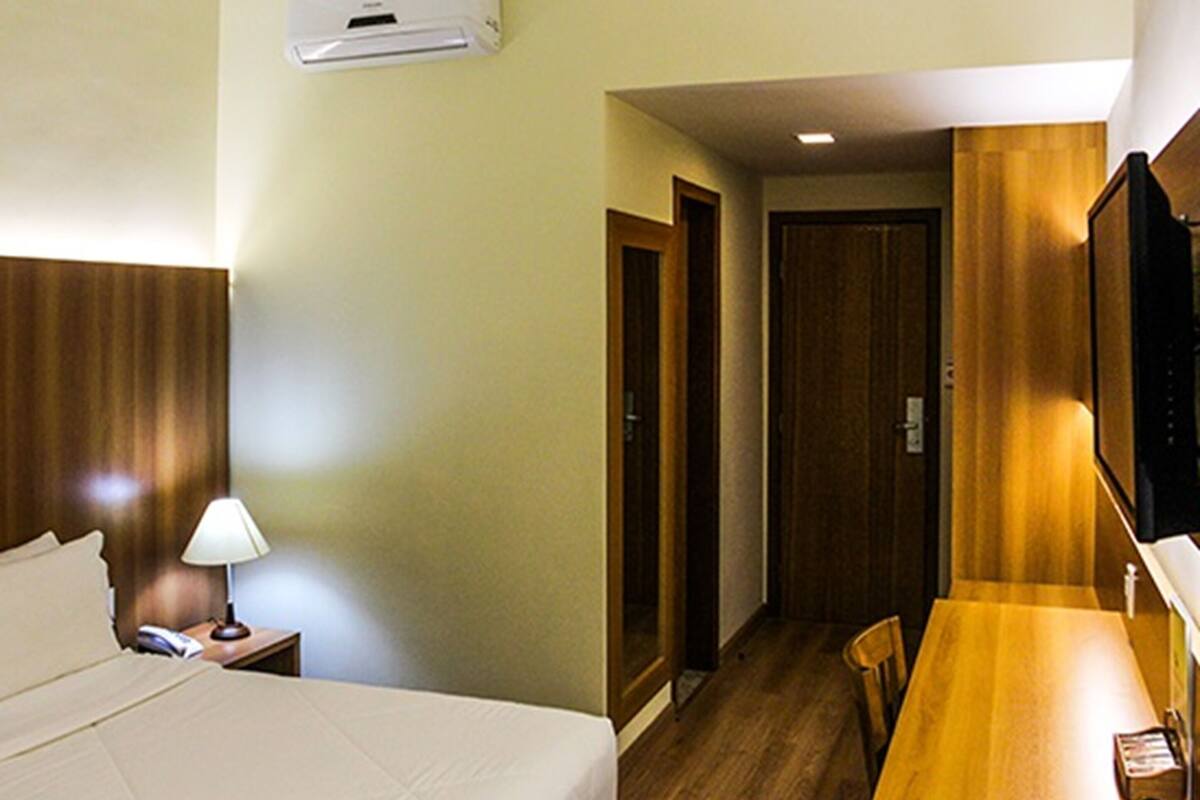 Une chambre d’hôtel comprenant un lit, une table de chevet, une lampe, une armoire en bois et un téléviseur.