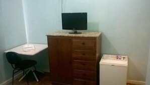 Una habitación pequeña con escritorio, una silla, un armario de madera y un refrigerador pequeño.