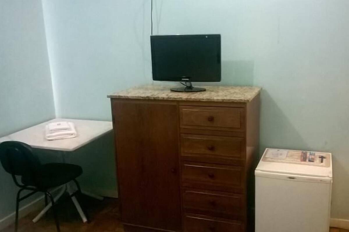 A small room with a desk, a chair, a wooden cabinet, and a small refrigerator.