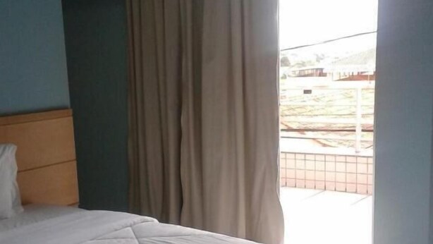 A hotel room with a bed, a pillow, a blanket, and a window with curtains.