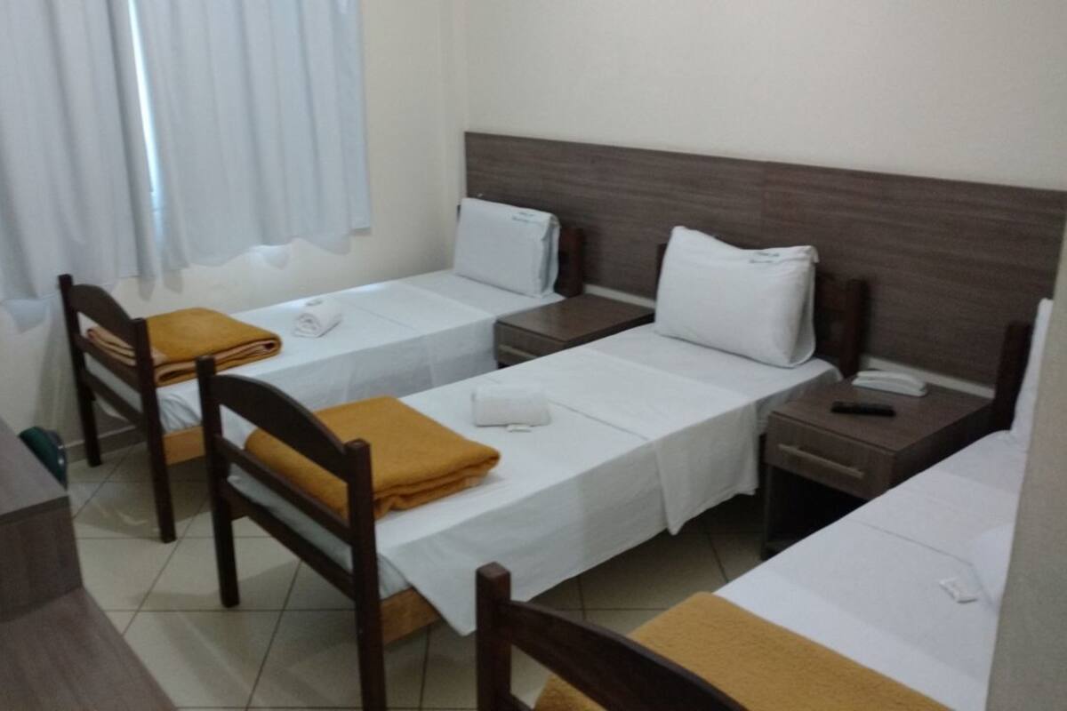 Habitación de hotel con dos camas individuales, una silla de madera, una mesita pequeña y una mesita de noche con teléfono.