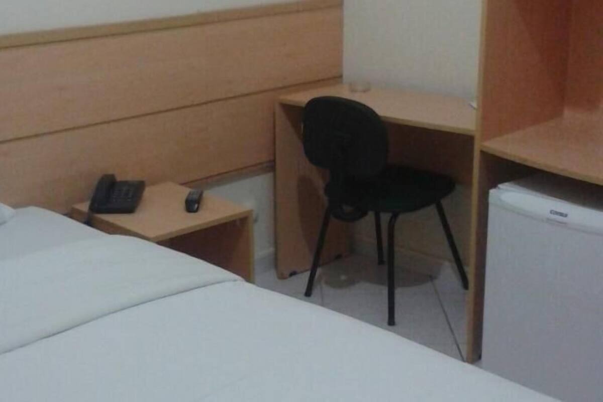 Habitación de hotel con cama, escritorio, silla, teléfono y refrigerador.