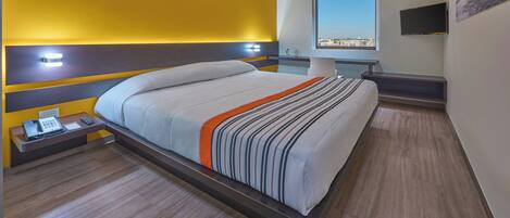 A modern hotel room with a bed, bedside table, and a TV mounted on the wall.