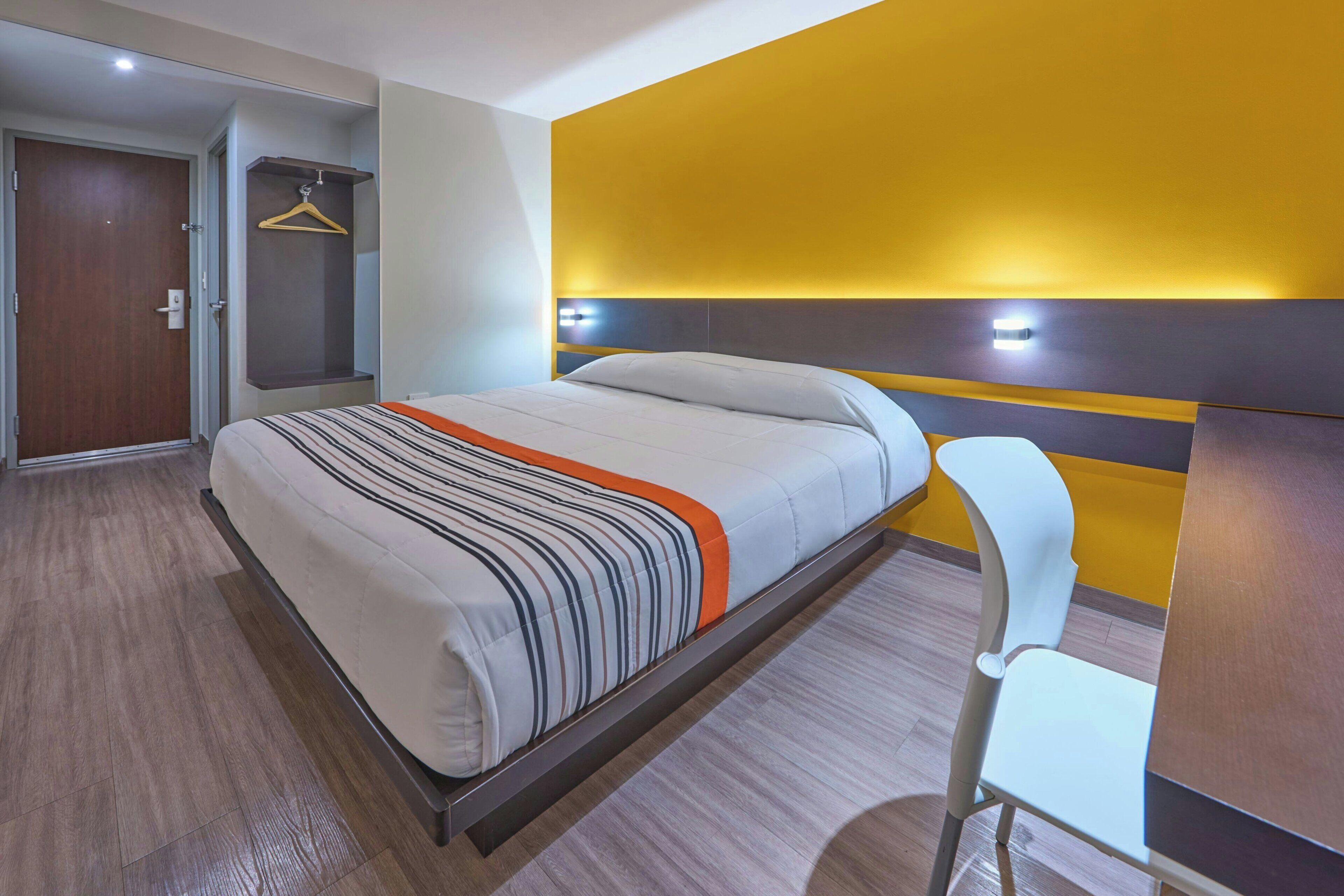 A hotel room with a bed, a chair, a wardrobe, and a door.
