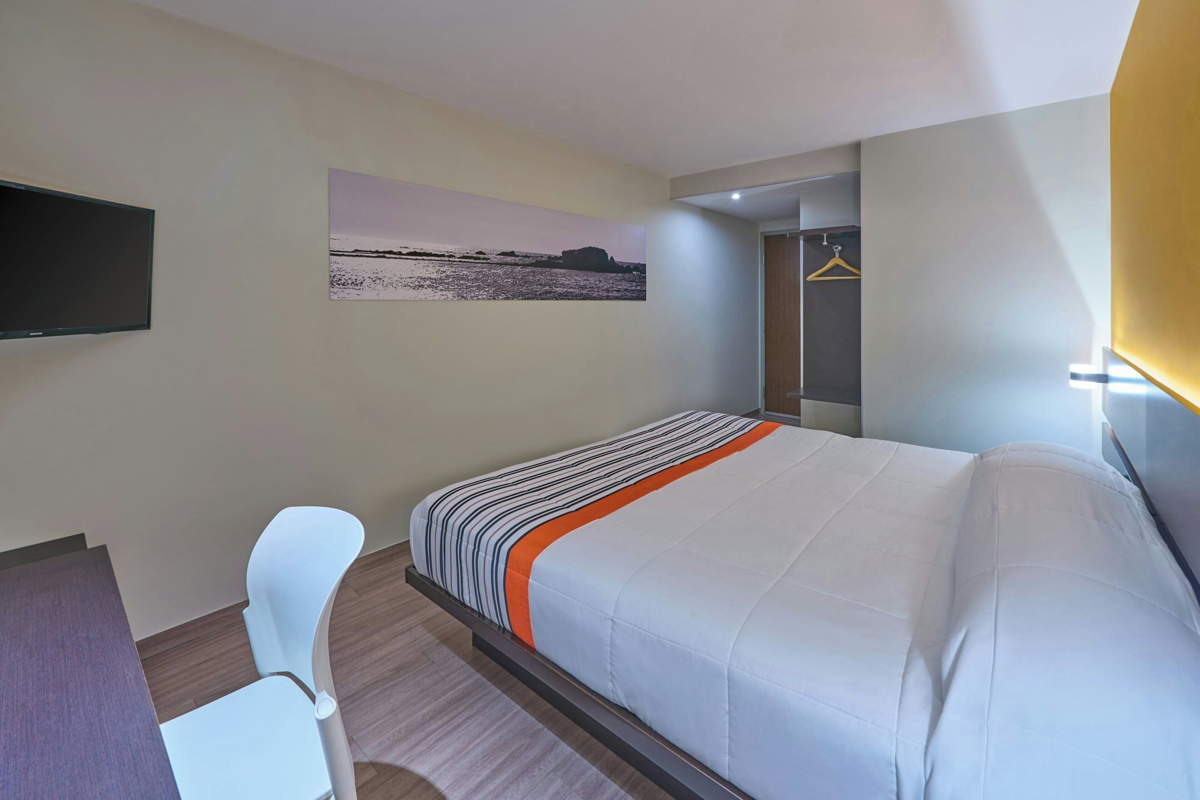 Une chambre d’hôtel avec un lit, un bureau, une chaise, une télévision et un tableau au mur.