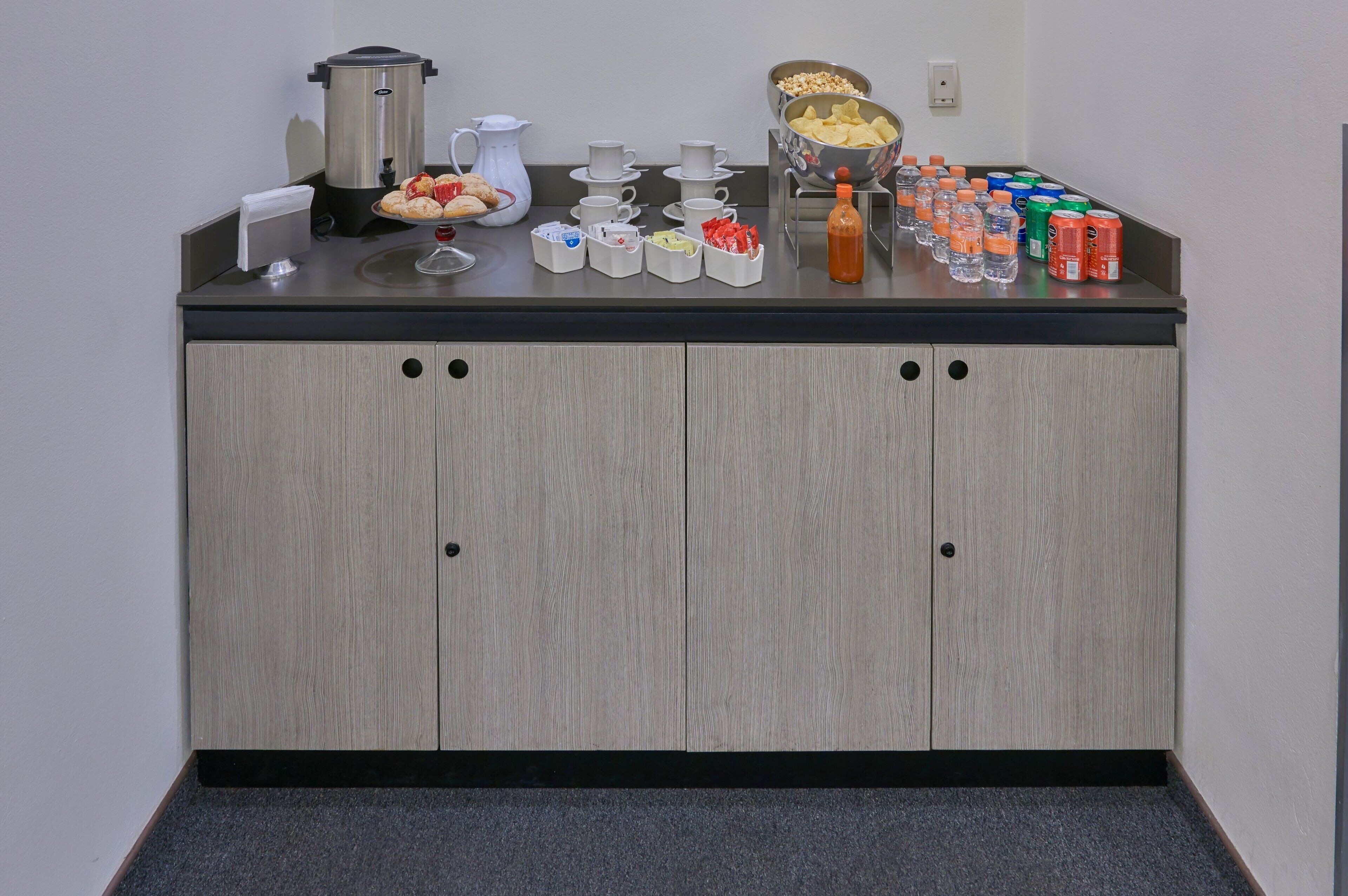 A breakfast bar with a coffee maker, teapot, cups, and a variety of snacks and beverages.