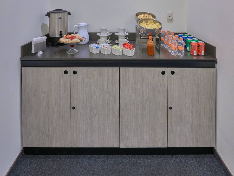 A breakfast bar with a coffee maker, teapot, cups, and a variety of snacks and beverages.