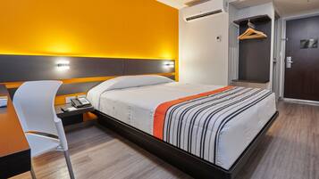 Quarto de hotel moderno com cama, mesa de cabeceira, cadeira e guarda-roupa.