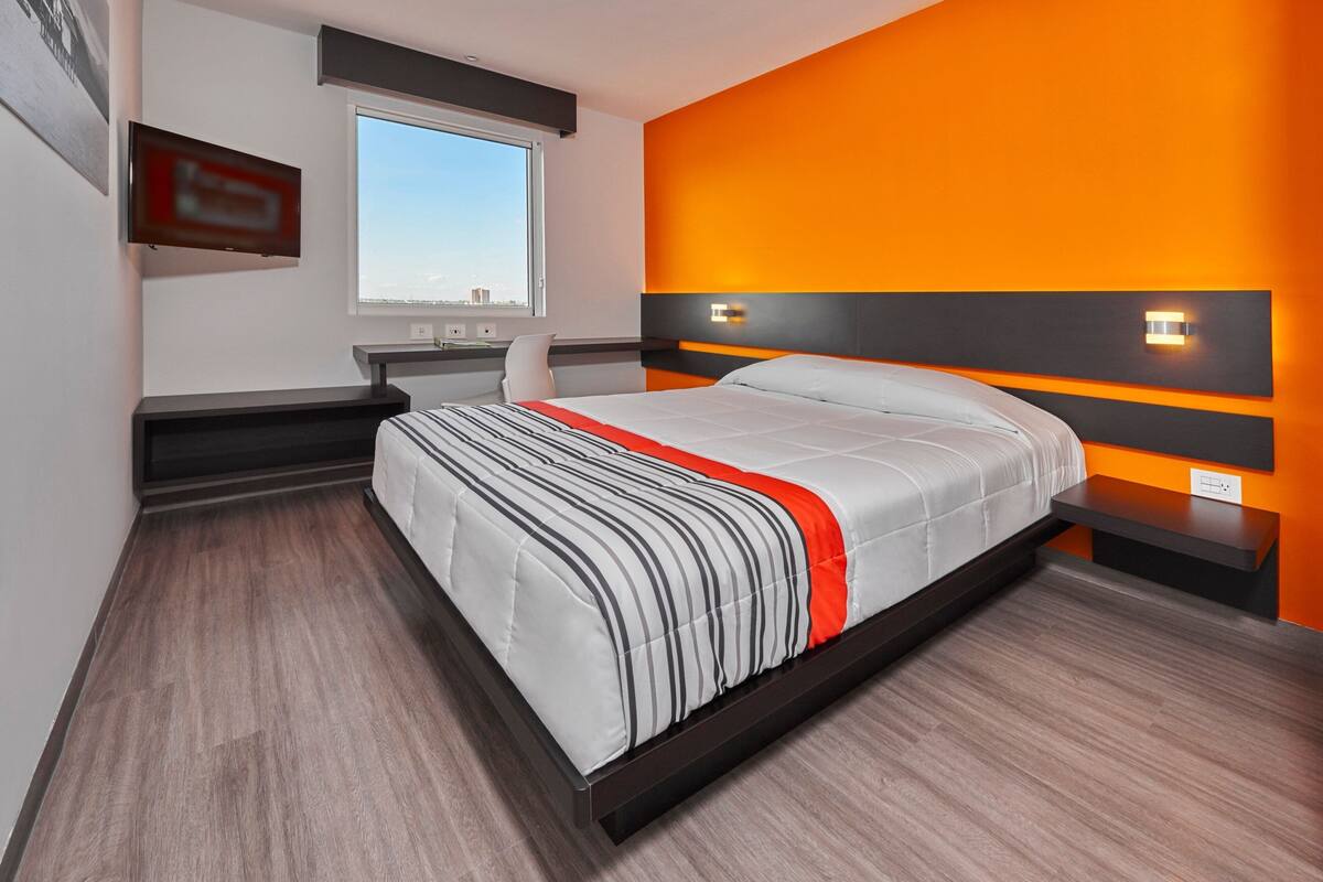 A modern hotel room with a large bed, a desk, and a window with a city view.