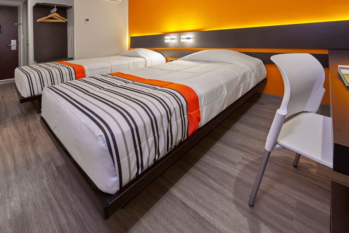 A hotel room with two beds, a white chair, and a wooden desk.