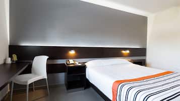 A modern hotel room with a bed, a desk, a chair, and a nightstand with a phone.