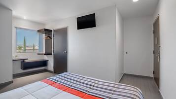 Una habitación de hotel moderna con una cama grande, un banco integrado, un televisor de pantalla plana y una ventana con vista a palmeras.